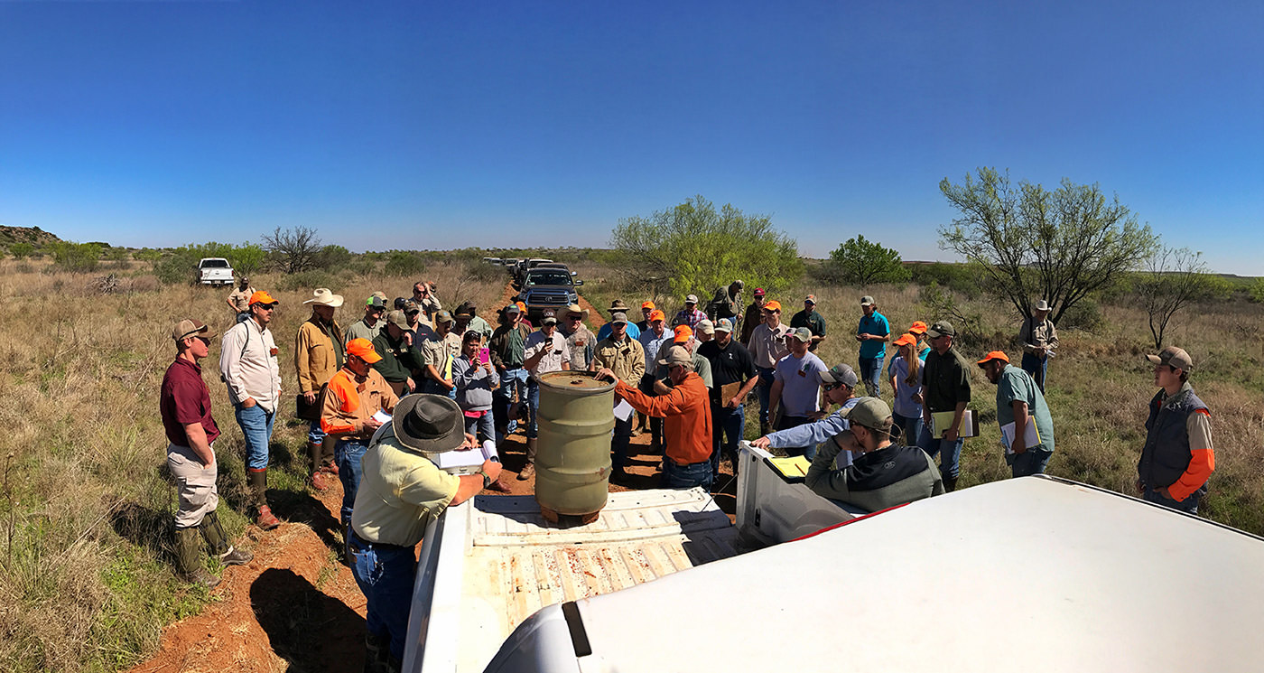 Outdoor event: Group of people gathered for a hunting or conservation meeting in a rural landscape.